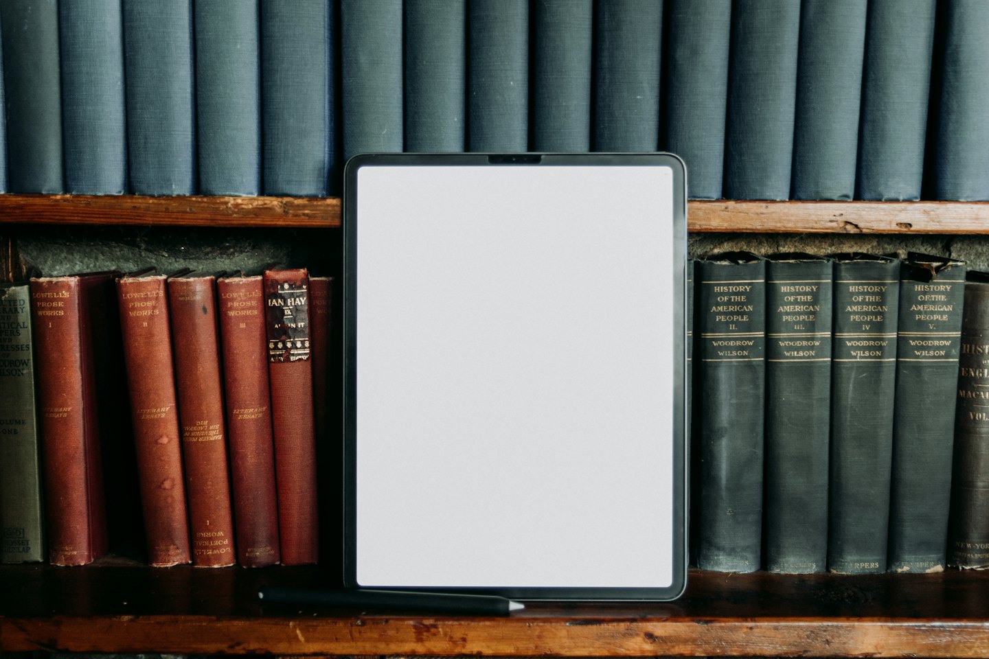 Tablet und alte Bücher in einem Holzregal.